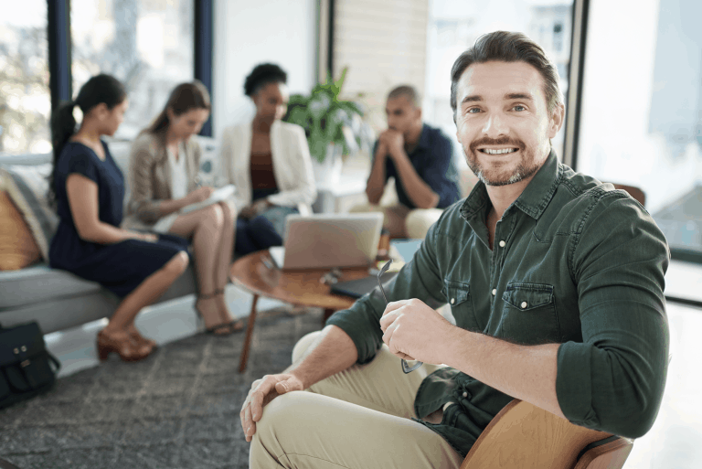Smiling man in foreground with team meeting in background.