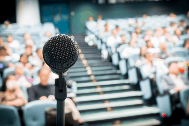 Microphone in focus with blurred audience in auditorium seats.