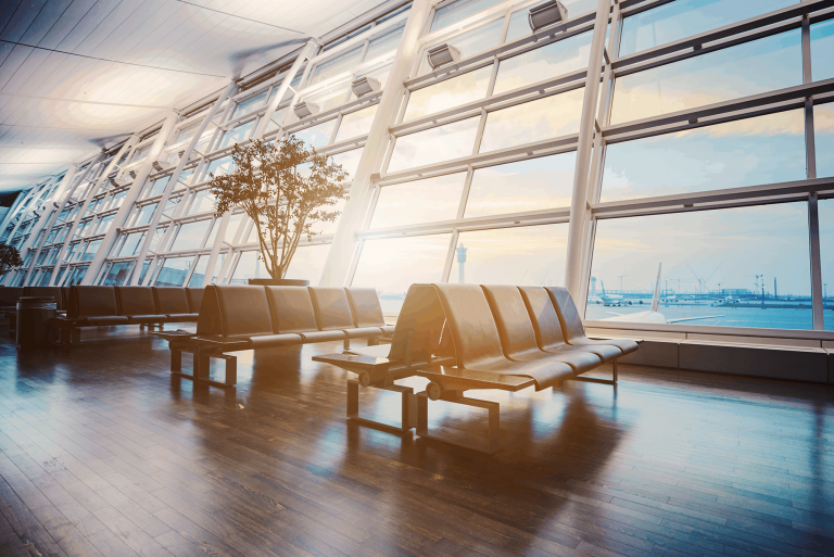 Empty airport terminal with seating and large windows at sunrise.